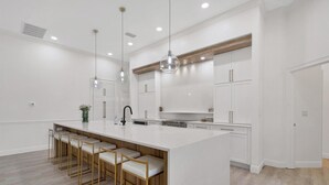 Une cuisine moderne dotée d’un grand îlot central, de tabourets de bar, de luminaires suspendus et de meubles blancs.
