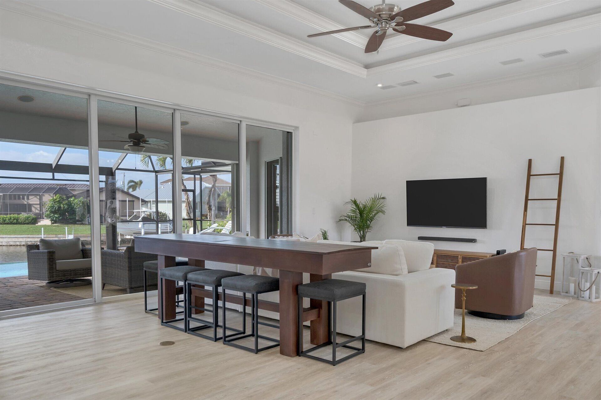 A modern living room with a bar area, a flat-screen TV, and a large sliding glass door leading to a pool area.