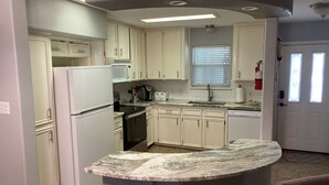 A kitchen with white cabinets, a refrigerator, a microwave, a stove, and a sink. There is a window with blinds and a door with a window.