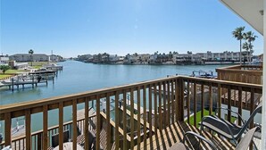 A waterfront view from a balcony with a wooden deck, overlooking a marina with boats and a row of buildings.
