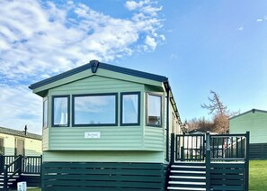 A green mobile home with a nameplate reading 'Sienna,' a fenced deck, and a clear sky. - 3 bedroom accommodation in Slaley, Hexham (Slaley, Hexham)