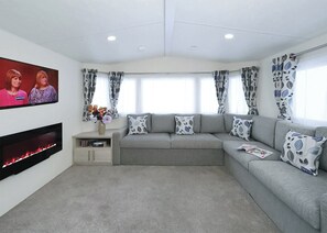Una sala de estar con un sofá gris, cojines estampados, un televisor de pantalla plana, una chimenea y cortinas con diseño.