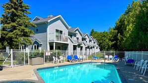 A swimming pool with lounge chairs and a fenced area, surrounded by a two-story building with a balcony. - Fish Creek, Door County Condo - Walk to Shopping, Dining & Peninsula State Park (Fish Creek)