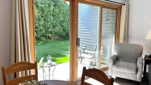 A room with a dining table, chairs, a lamp, and a view of a garden through a sliding glass door. - Fish Creek, Door County Condo - Walk to Shopping, Dining & Peninsula State Park (Fish Creek)