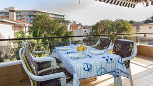 A balcony with a table set for two, chairs with floral upholstery, and a view of surrounding buildings and trees. - Venecia by Interhome (Playa de Aro)