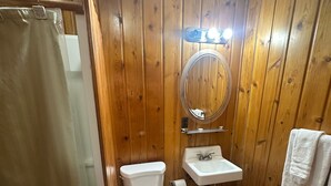 A bathroom with wooden walls, a toilet, a sink, and a shower curtain. - Country Cabin Motel (Quincy)