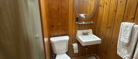 A bathroom with wooden walls, a toilet, a sink, and a shower curtain.