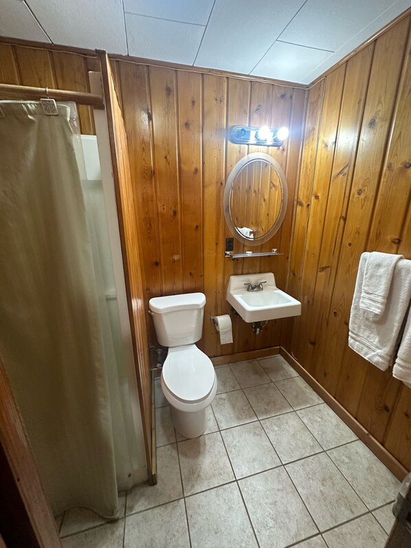 A bathroom with wooden walls, a toilet, a sink, and a shower curtain.