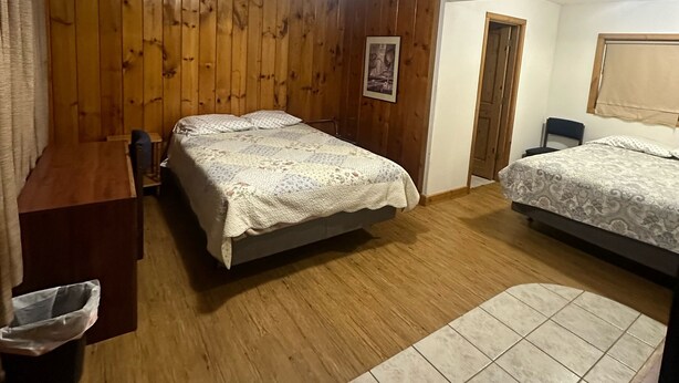 A bedroom with two beds, wooden walls, a desk, and a tiled floor. - Country Cabin Motel (Quincy)