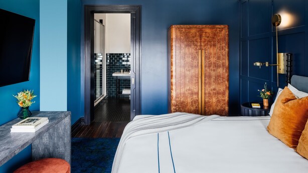 Un dormitorio moderno con una cama grande, un escritorio y un baño visible a través de una puerta abierta.