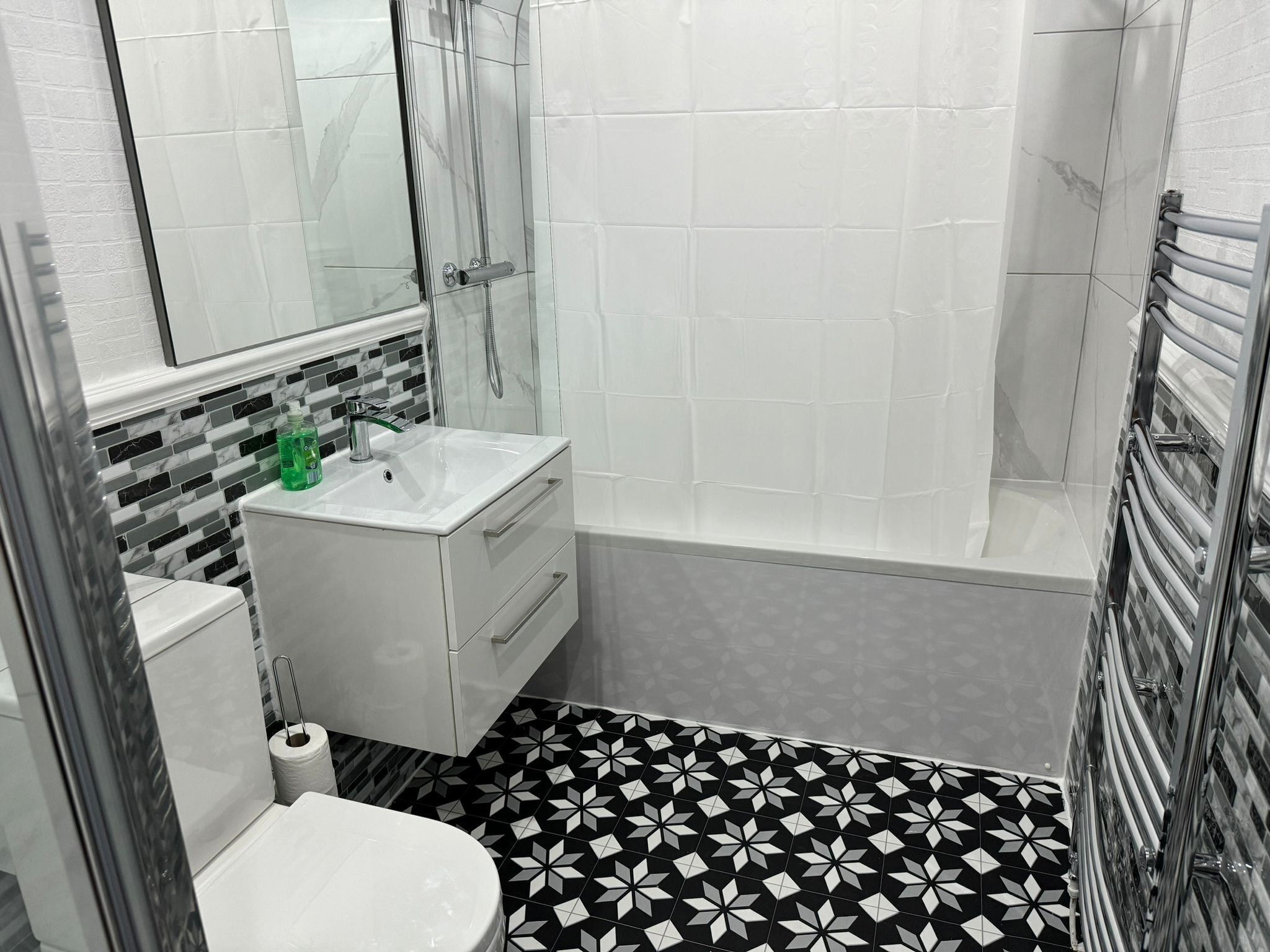 Une salle de bain avec un lavabo blanc, des toilettes, une douche et un carrelage décoratif.