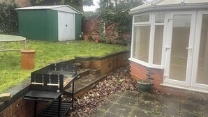 A backyard with a barbecue grill, a shed, a conservatory, and a brick wall. - 4 Bedroom House - Sleeps 6 - Garden, Bbq, Parking (Birmingham)