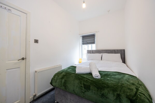 A bedroom with a bed, a radiator, a window with blinds, and a door.