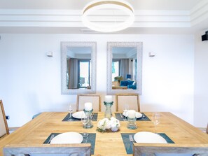Une salle à manger avec une table en bois dressée pour quatre personnes, deux grands miroirs sur le mur et, au fond, une vue sur un canapé bleu.