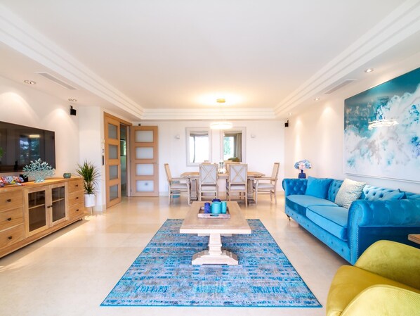 Un salon spacieux avec un canapé bleu, une table basse en bois et un coin repas comprenant une table et des chaises en bois.