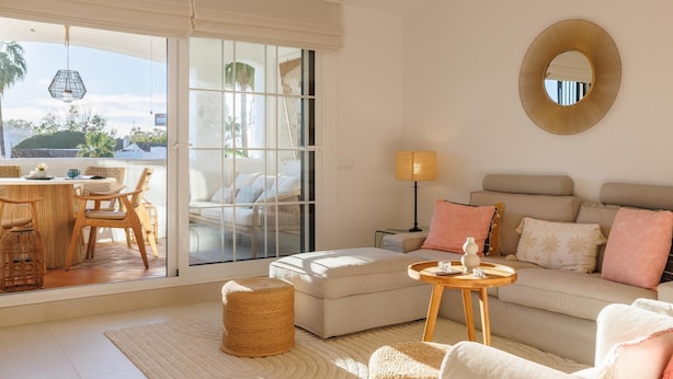 A living room with a sofa, a small round table, a lamp, and a large window with a view of the outdoors.