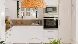 A modern kitchen with white cabinets, a microwave, an oven, and a hanging woven light fixture.