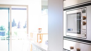 A modern kitchen with a built-in oven and microwave, a sliding glass door leading to a balcony, and a dining area with a table and chairs. - Jardines del Príncipe Golden Mile Suite Apartment (Marbella Golden Mile)