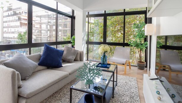 Ein modernes Wohnzimmer mit einer Couch, einem Couchtisch und Sesseln. Große Fenster bieten Blick auf die Stadt.