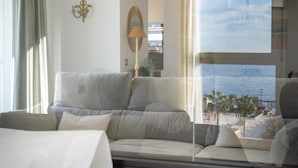 Een moderne woonkamer met een bank, een lamp en uitzicht op zee door een groot raam.