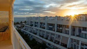 Een modern gebouw met meerdere balkons en uitzicht op zee bij zonsondergang.