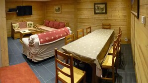 A wooden cabin with a dining table, chairs, a sofa, and a bed.