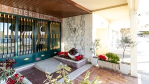 L’entrée d’un hôtel, avec un mur de marbre, une porte verte dotée de poignées en laiton et des plantes en pot.