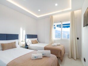 Hotellihuone, jossa on kaksi sänkyä, suuri ikkuna, josta on näkymä risteilyalukseen, ja kattoon upotetut valaisimet.
