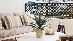 Un balcon avec un canapé, une plante en pot, des bougies et un panier en osier.