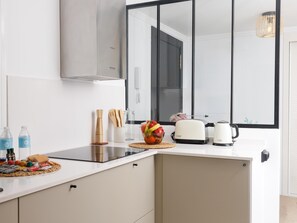 Una cocina moderna con encimera blanca, un tostador, una tetera y un cuenco con fruta.