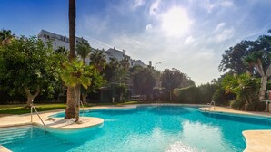 Une piscine à l’eau d’un bleu cristallin, entourée de palmiers et avec un bâtiment visible au loin.