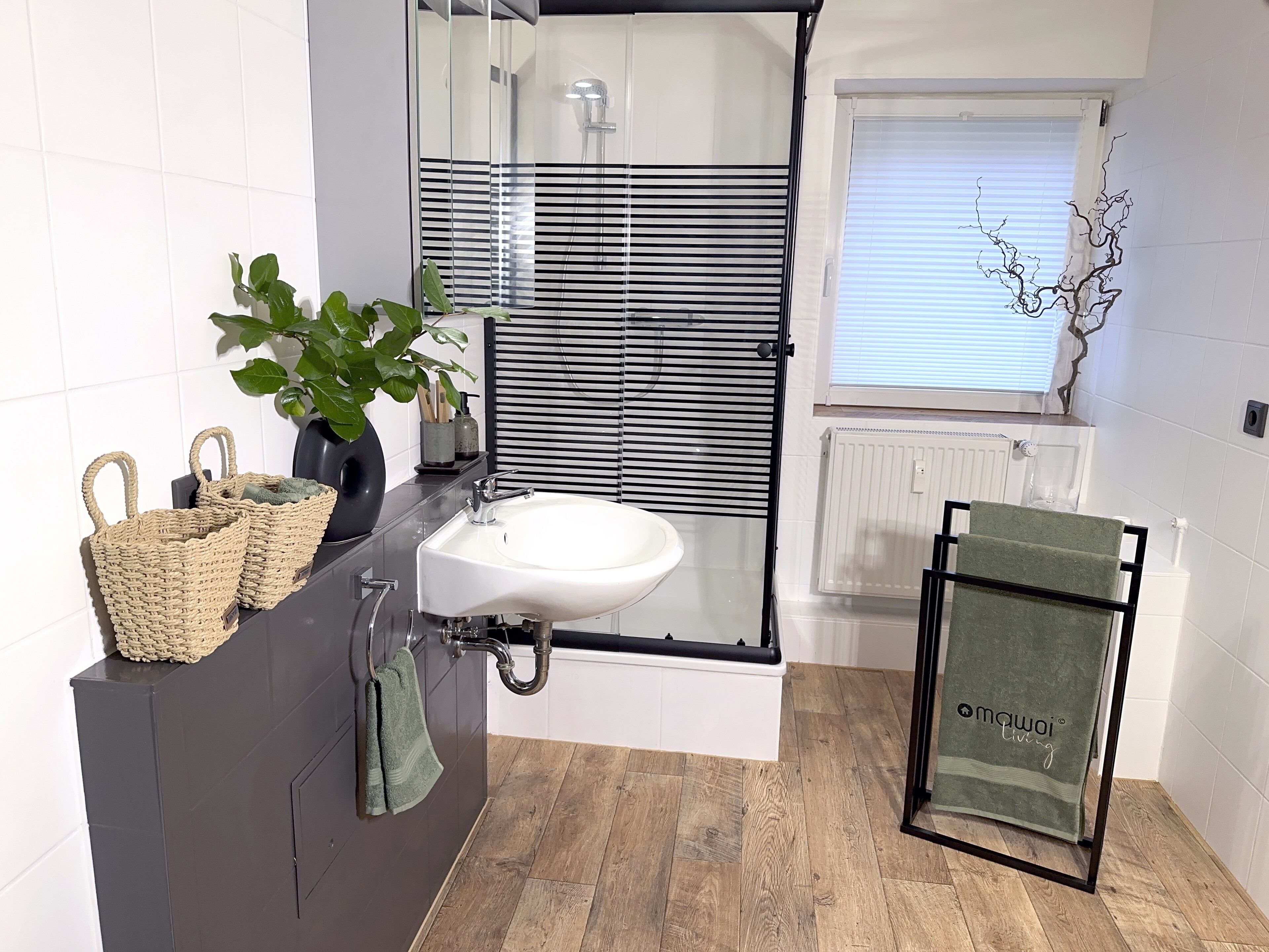 A modern bathroom with a glass shower enclosure, a white sink, and a wooden floor.