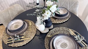 A round dining table set with dark plates, gold cutlery, and woven placemats.
