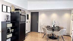 A modern kitchen with a built-in oven, a coffee machine, and a dining area with a round table and two chairs.