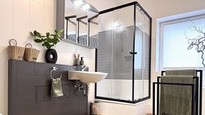 A modern bathroom with a grey vanity, a white sink, and a glass shower enclosure.