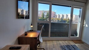 En modern lägenhet med en stor skjutdörr i glas som leder ut till en balkong, ett skrivbord med en lampa och utsikt över staden.
