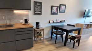 Ett modernt kök med en bänkskiva i trä, en diskho i rostfritt stål och en kaffemaskin. Det finns ett matbord med stolar och ett litet skåp med en växt i.