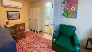 A room with a bed, a desk, a chair, a colorful rug, a green armchair, a wardrobe, and a painting on the wall. - 2 bed 1 bath cottage home (Price)