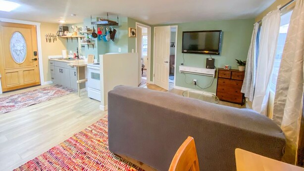 A compact living space with a kitchenette, a television mounted on the wall, and a patterned rug. - 2 bed 1 bath cottage home (Price)