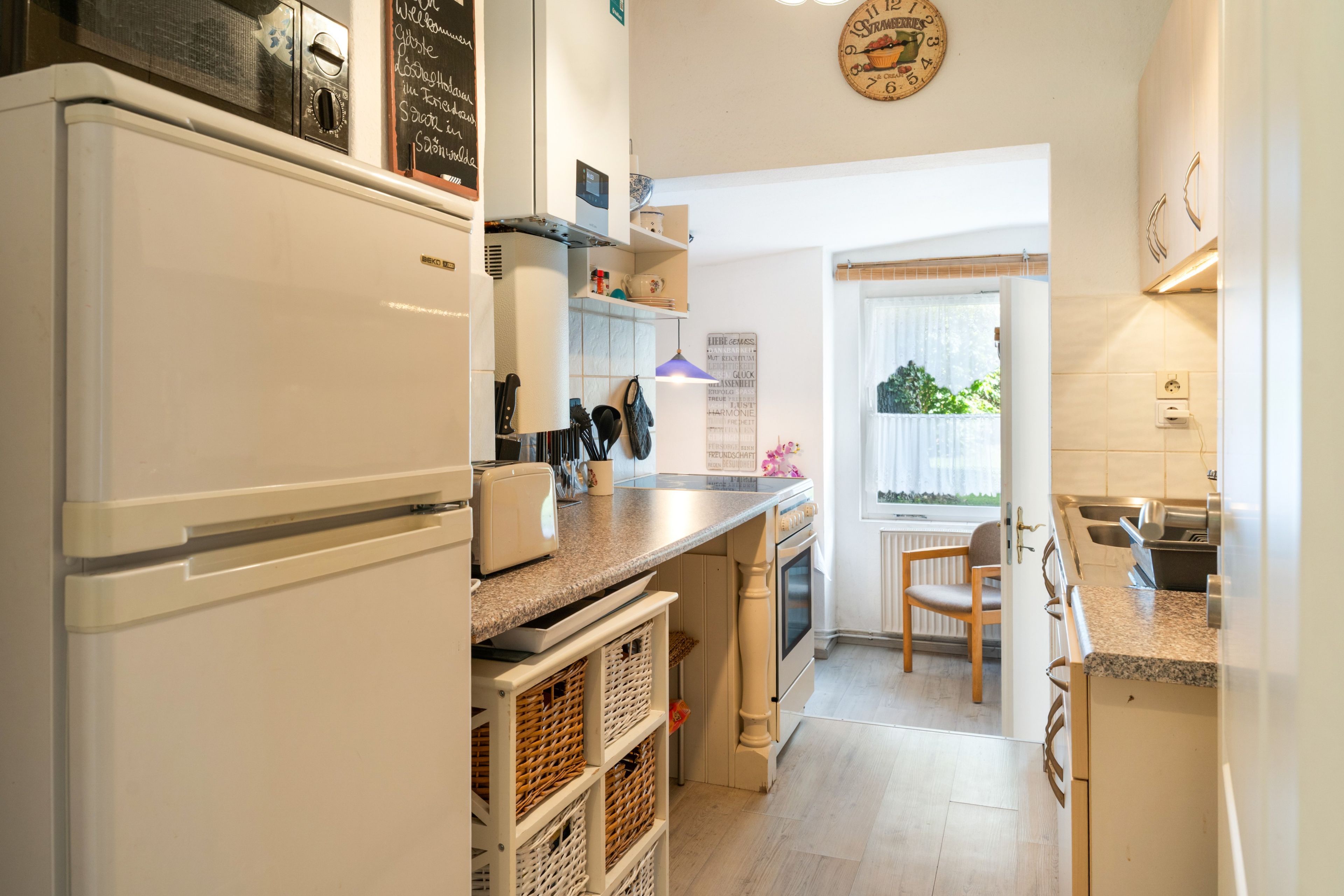 Una cocina con refrigerador, estufa y ventana con vista a follaje.