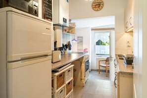 Una cocina con refrigerador, estufa y ventana con vista a follaje.