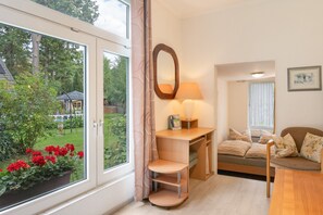 Ein Zimmer mit einem großen Fenster, einem Schreibtisch mit Lampe, einer Couch und einem Spiegel an der Wand.