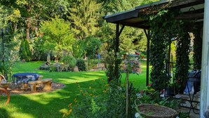Un jardin avec un banc en pierre, un arbre et une pergola recouverte de plantes grimpantes.