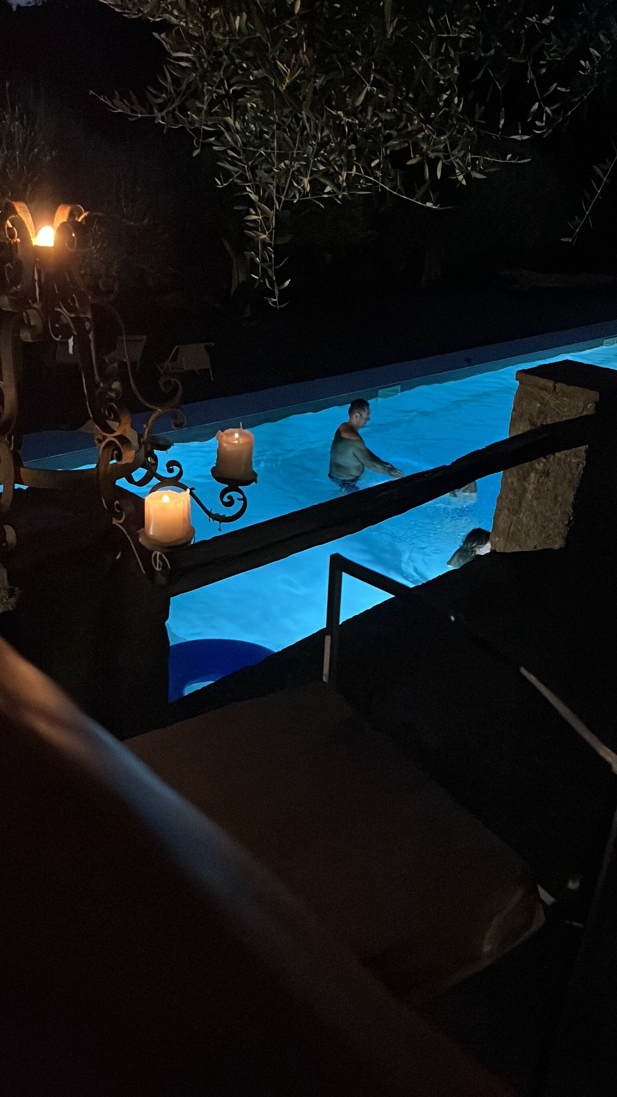 Vista nocturna de una piscina con una persona nadando, rodeada por un entorno oscuro y frondoso.