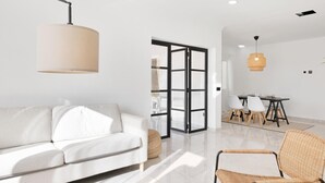 Un salon moderne avec un canapé blanc, des fauteuils en osier, une table à manger avec des chaises et une grande fenêtre.