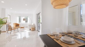 Un espace de salle à manger moderne avec une table noire dressée pour quatre personnes, des chaises blanches et un grand luminaire suspendu en forme de suspension tressée.