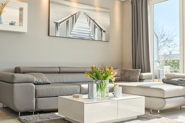 A modern living room with a grey sofa, a white coffee table, and a painting of a bridge.