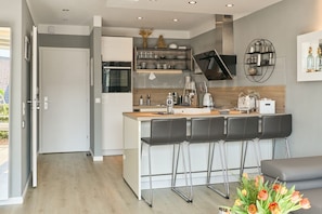 A modern kitchen with a central island, bar stools, and a dining area with a grey sofa.