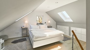 A modern bedroom with a sloped ceiling, skylight, a large bed, bedside tables with lamps, and built-in storage cabinets.