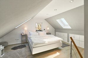 A modern bedroom with a sloped ceiling, skylight, a large bed, bedside tables with lamps, and built-in storage cabinets.